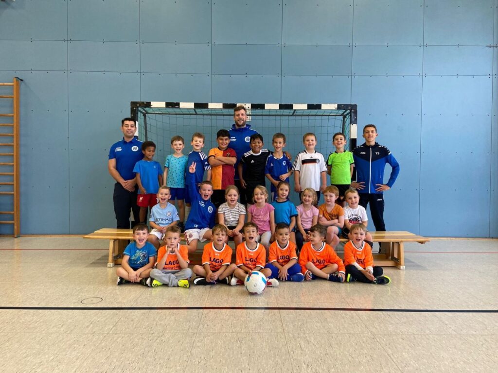 Gruppenfoto in einer Turnhalle mit mehreren jugendlichen Fußballspielern in unterschiedlicher Kleidung vor einem Hallentor stehend