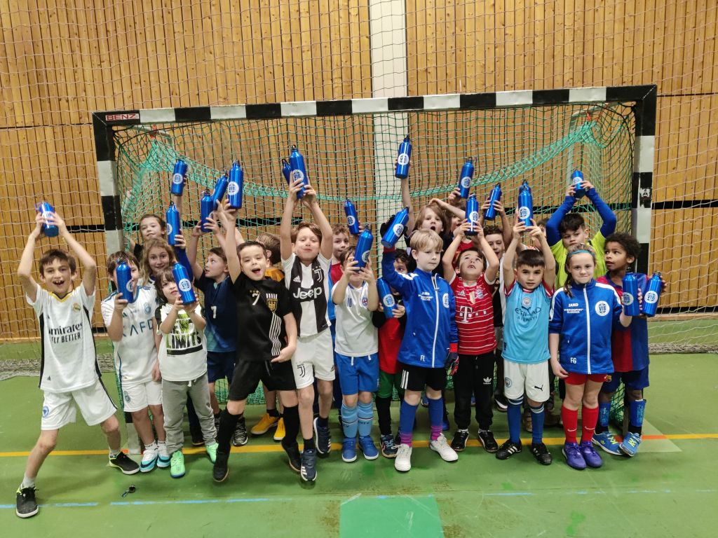 Gruppenbild jubelnder jugendlicher Fßballspieler vor einem Hallentor mit blauen Trinkflaschen in die Luft hebend