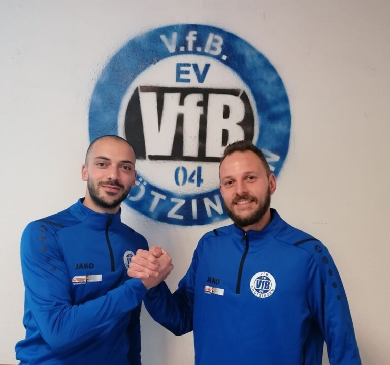 Handshake von zwei Personen in blauer Vereinskleidung vor dem Logo des VfB Groetzingen stehend